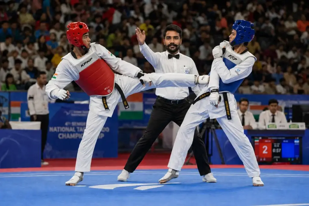 Two taekwondo athletes in protective gear compete in a match with a referee overseeing.